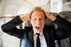 Fear of flight. Shocked mature businessman touching his head with hands and looking at camera while sitting at his seat in airplane