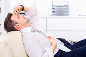 Mid-adult businessman lying on couch at office, looking exhausted eyes closed. Bright background. Click here for more business photos: